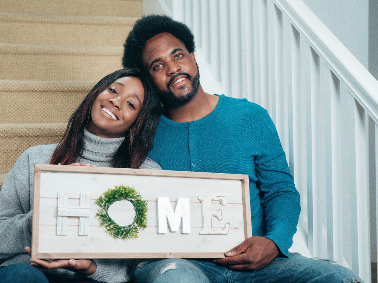 The Art of Drawing Readers In: Your attractive post title goes here Smiling couple sitting on stairs holding a HOME sign, symbolizing new beginnings in their new house.