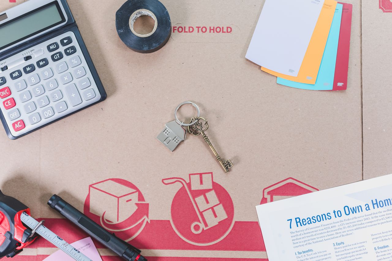 Flat lay of home buying essentials with calculator, keys, tape, and color swatches.